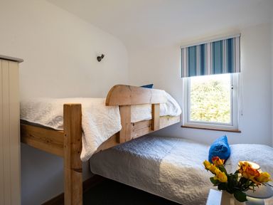 A bedroom with bunk beds, white bedding, a blue striped window blind, and yellow flowers at Harbour Lodge Port Isaac
