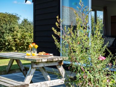 A wooden picnic table outside with two glasses of orange juice a plate of pastries and strawberries and a vase of flowers at Harbour Lodge in Port Isaac