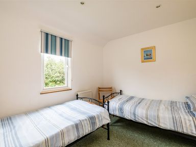 A bedroom with two single beds a window with striped blinds and a wooden chair at Puffin Lodge in Port Isaac