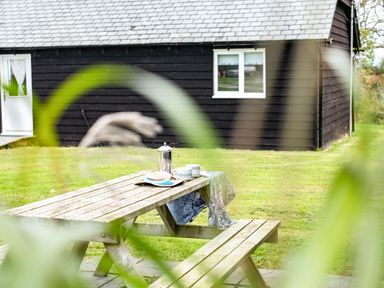 A wooden picnic table with a tablecloth cups and a French press on the lawn outside a black house at Puffin Lodge in Port Isaac