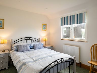 A bedroom with a double bed between two nightstands with lamps and a window with striped blinds at Dolphin Lodge in Port Isaac