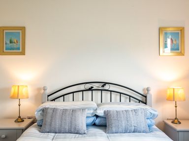 A bedroom with a bed with striped bedding two bedside tables with lamps and two framed paintings on the wall at Dolphin Lodge in Port Isaac