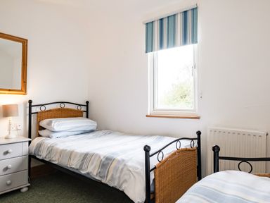 A bedroom with two single beds a nightstand with a lamp a window with blue striped blind and a mirror on the wall at Dolphin Lodge in Port Isaac