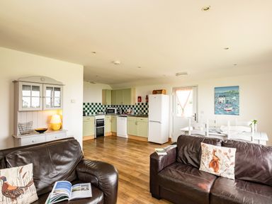 An open living area with brown leather sofas a kitchen with green cabinets and a dining table with white chairs at Dolphin Lodge in Port Isaac