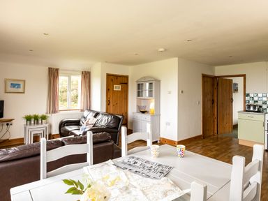 A living room with brown leather sofas a white dining table with colorful mugs and a map and a kitchen area at Dolphin Lodge in Port Isaac