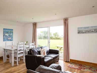 A living room with leather sofas white dining table with chairs and sliding glass door at Dolphin Lodge in Port Isaac