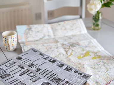 A table with a map, a brochure, a colorful mug, and a vase with white flowers at Dolphin Lodge in Port Isaac