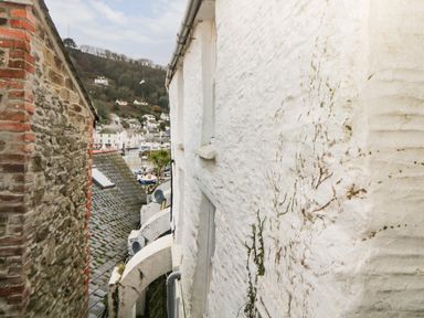A view between two buildings showing rooftops and houses on a hillside with boats in a harbor at Spindrift in Polperro
