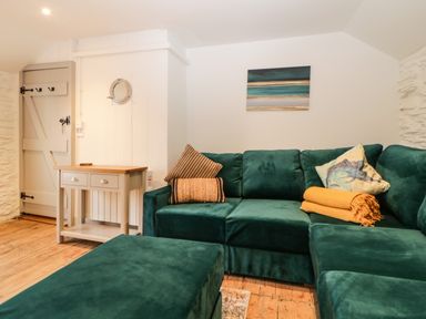 A living room with a green sectional sofa orange throw and wooden side table at Spindrift in Polperro