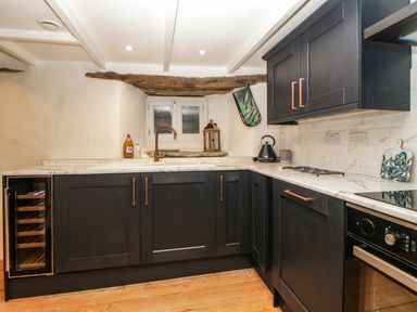 A kitchen with black cabinets white countertops a small window above the sink and wooden floor at Spindrift in Polperro