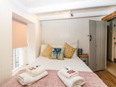 A bedroom with a double bed with pillows and folded towels on a blanket by a window with a blind at Spindrift in Polperro