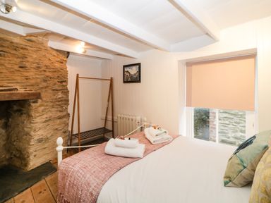 A bedroom with a bed with pillows and folded towels near a stone fireplace and window at Spindrift Polperro