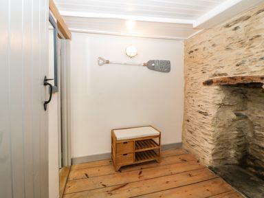 A room with wooden floor a small bench a paddle on the wall and a stone fireplace at Spindrift in Polperro