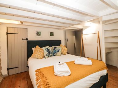 A bedroom with a bed with decorative pillows and folded towels on a blanket at Spindrift in Polperro