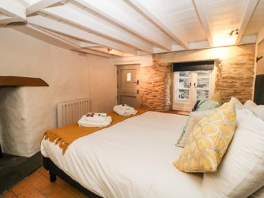 A bedroom with a bed with yellow pillows and folded towels near a window with stone walls at Spindrift Polperro