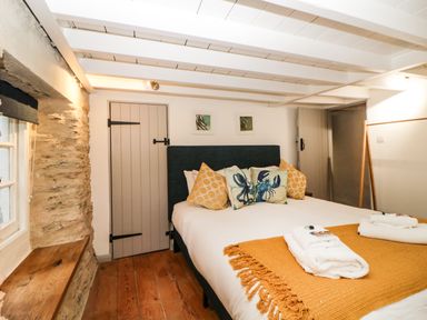 A bedroom with a bed with orange and crab pattern pillows and folded towels on a blanket at Spindrift in Polperro