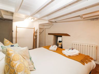 A bedroom with a double bed, cushions, folded towels, a mirror, a radiator, and wooden beams on the ceiling at Spindrift in Polperro