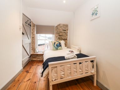 A small bedroom with a single bed near a window and wooden door at Spindrift in Polperro