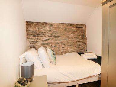 A small bedroom with a bed against a stone wall bedside table with a lamp and folded towels on the bed at Spindrift Polperro
