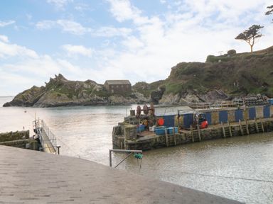 A harbor area with a pier a small building on rocky land and water at Spindrift in Polperro