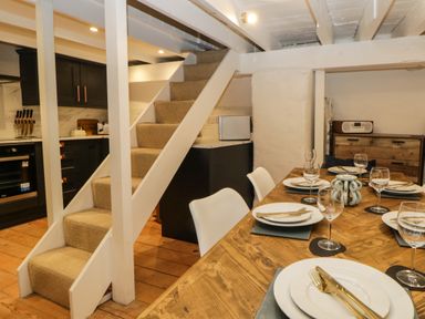 A dining table set with plates and glasses next to carpeted stairs and a kitchen area at Spindrift in Polperro