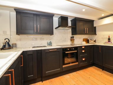 A kitchen with black cabinets white counters and wooden floor at Spindrift Polperro