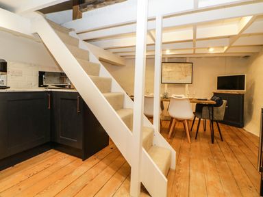 A room with a staircase next to a kitchen corner and a dining table with chairs at Spindrift in Polperro