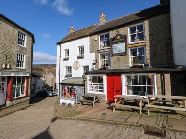 A street view with old stone buildings a red door and wooden picnic tables at Cross View Cottage in Alston