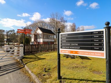 A railway crossing with a signal box building and multiple closed facility signs at Cross View Cottage in Alston