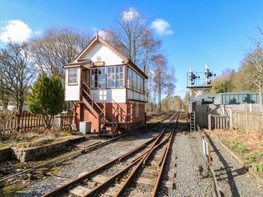 A railway signal box beside train tracks with trees and fencing in Alston