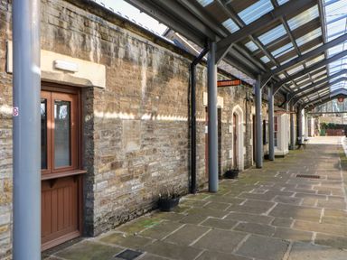 An outdoor covered walkway with stone walls and doors labeled toilets and ticket office at Cross View Cottage in Alston