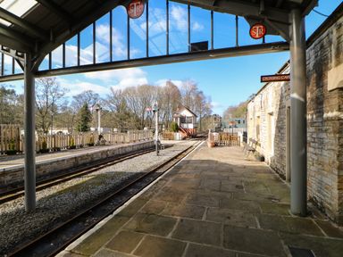 A train platform with tracks benches and a stone building with a sign reading Crossing Cafe at Cross View Cottage in Alston