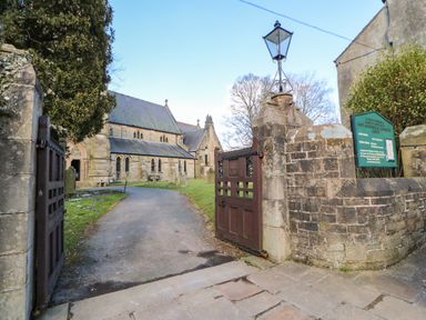 An open gate leading to a stone church with a paved path and grassy area with gravestones at Cross View Cottage in Alston