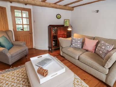 A living room with a beige sofa and patterned cushions a gray armchair a wooden cabinet and a white tray on an ottoman at Cross View Cottage in Alston
