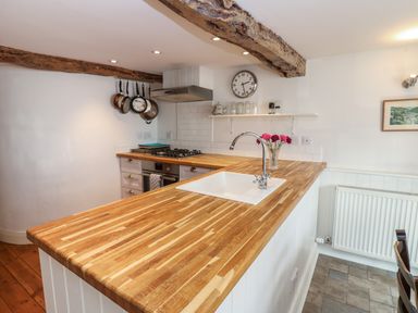 A kitchen with wooden countertop and sink and hanging pans above stove at Cross View Cottage in Alston