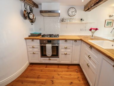 A kitchen with white cabinets wooden countertops a gas stove an oven a sink and hanging pans at Cross View Cottage in Alston