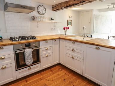 A kitchen with wooden floors white cabinets a gas stove an oven a sink and a vase with flowers at Cross View Cottage in Alston