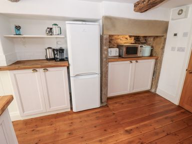 A kitchen area with wooden floor white cabinets a white fridge a microwave toaster kettle and coffee maker at Cross View Cottage in Alston