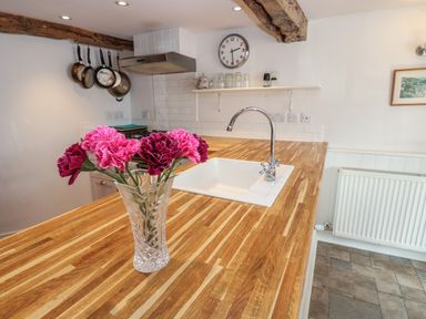 A kitchen with a wooden countertop and a vase with flowers near a sink at Cross View Cottage in Alston