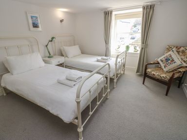 A bedroom with two single beds a nightstand with a lamp a window with curtains and a floral armchair at Cross View Cottage in Alston