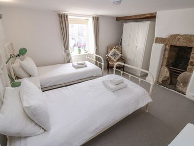 A bedroom with two single beds a wardrobe a chair and a fireplace at Cross View Cottage in Alston