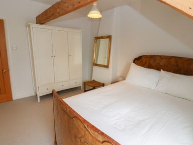 A bedroom with a wooden bed with white bedding a white wardrobe a wooden door a small stool and a gold framed mirror at Cross View Cottage in Alston