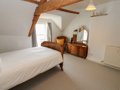 A bedroom with a wooden bed a dresser with a mirror an armchair and exposed ceiling beams at Cross View Cottage in Alston