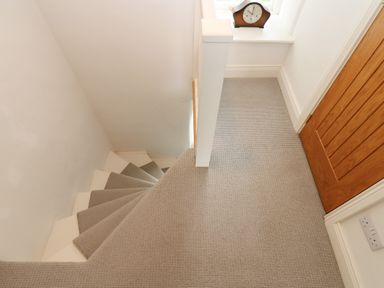A carpeted staircase with beige carpet a wooden door and a clock on the window ledge at Cross View Cottage in Alston