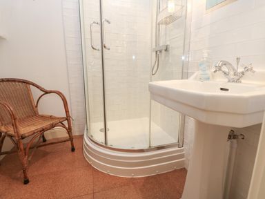 A bathroom with a corner shower enclosure a white pedestal sink and a wicker chair at Cross View Cottage in Alston