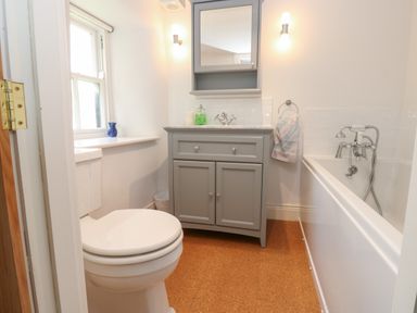A bathroom with a toilet a gray sink cabinet with mirror and two wall lights and a bathtub at Cross View Cottage in Alston