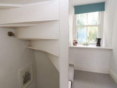 A stairwell with white painted stairs a framed picture on the wall and a window with decorative items on the sill at Cross View Cottage in Alston