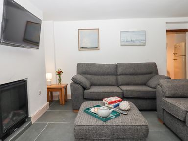 A living room with gray sofas a wall-mounted tv a fireplace and a wooden side table with a lamp at Beach Road House Hele Bay Ilfracombe