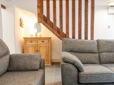 A living room with two grey sofas wooden cabinet lamp and wooden staircase at Beach Road House Hele Bay Ilfracombe