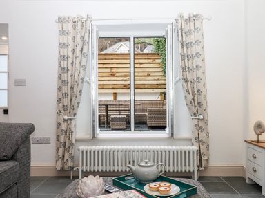 A window with floral curtains open to a patio with wicker furniture in a living room at Beach Road House in Hele Bay Ilfracombe